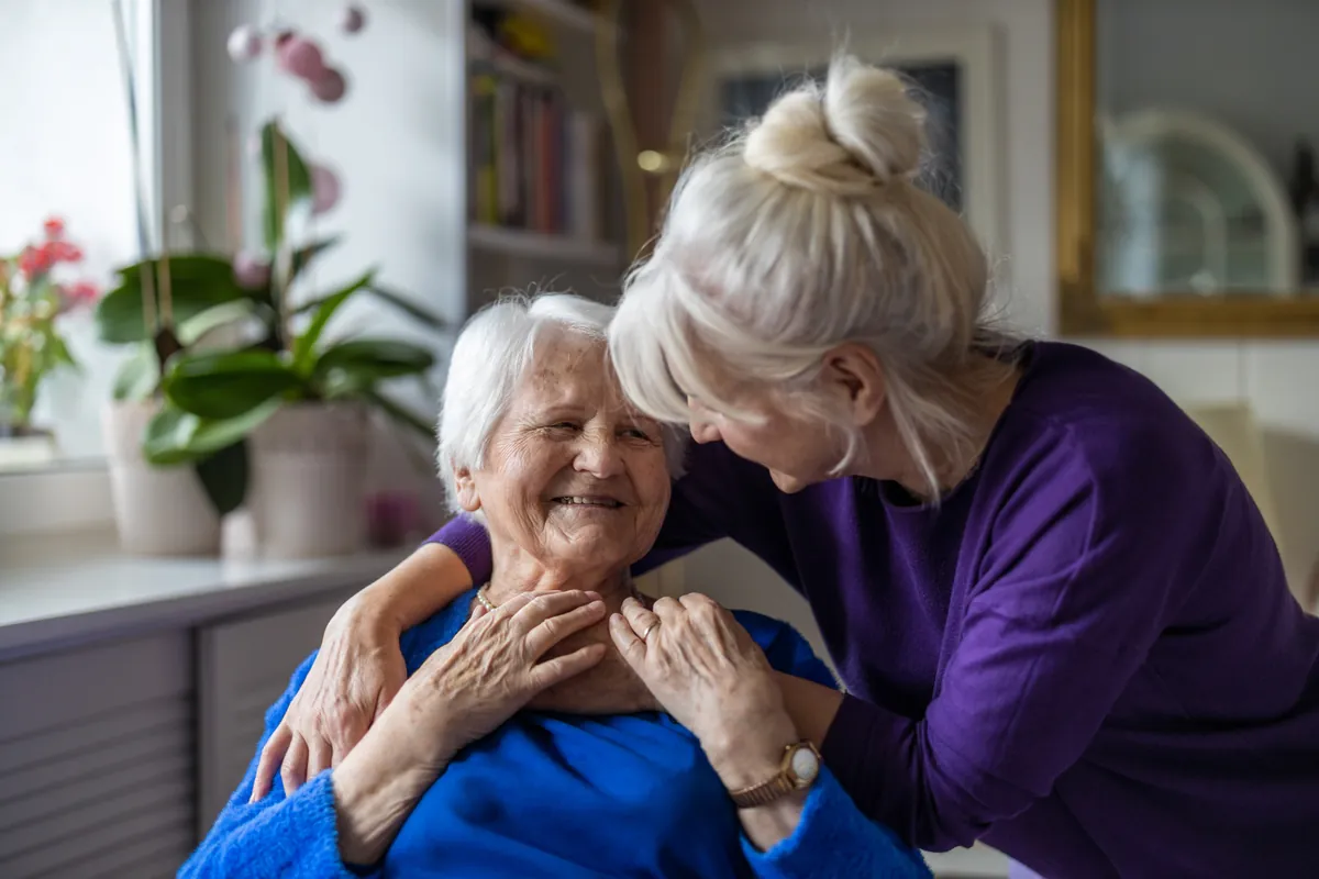 Adult daughter tenderly hugging her smiling elderly mother